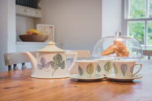 Table with tea pot , cups and saucers and croissants in a cake stand.