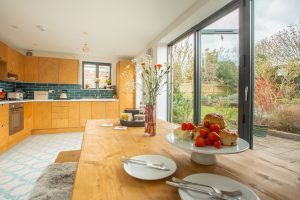 View of kitchen from dining area with bi-folding doors on the right. A cake stand on the table with scones and strawberries