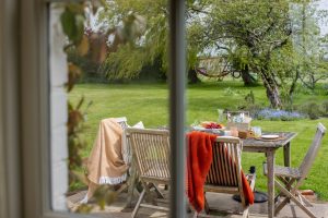 Image from inside to the outdoors with table and chairs and drinks and cake on the table