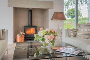 Image of a coffee table with a vase and flowers and a wood burner lit in the background