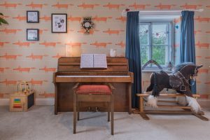 Image of a piano with a rocking horse to the right in front of a window