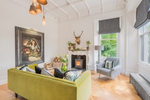 Image of a lounge with the fireplace lit window to the right and large picture to the wall on the left.